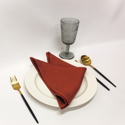 Conjunto de louça branca com guardanapo castanho, copo texturizado e talheres pretos e dourados