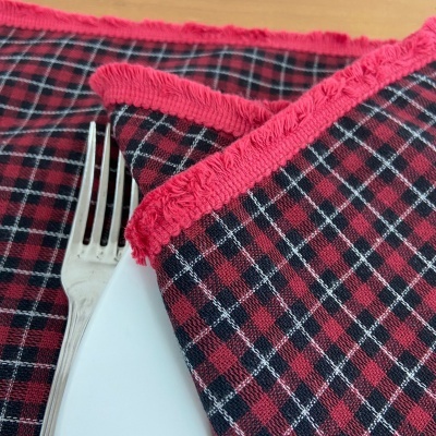 Guardanapo de tecido xadrez vermelho, preto e branco com franja vermelha sobre prato com garfo