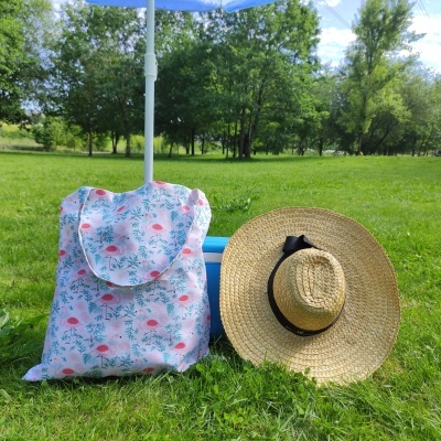 Mochila estampada de flamingos e chapéu de palha junto à relva e guarda-sol azul