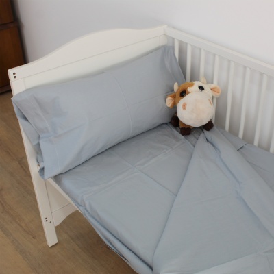 Cama infantil branca com roupa de cama cinza clara e peluche de vaca castanha e branca