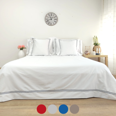 Cama arrumada com edredão branco e almofadas, relógio na parede e mesa de cabeceira com decoração