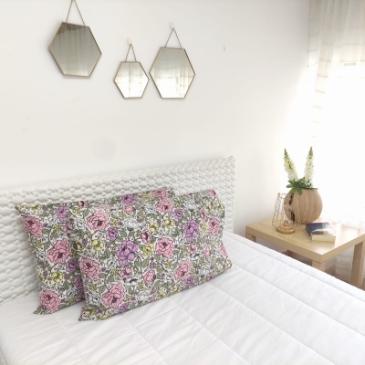 Almofadas florais coloridas sobre cama branca com cabeceira texturizada e mesa com vaso