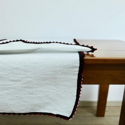 Toalha de mesa branca texturizada com bordado preto e vermelho numa mesa de madeira.