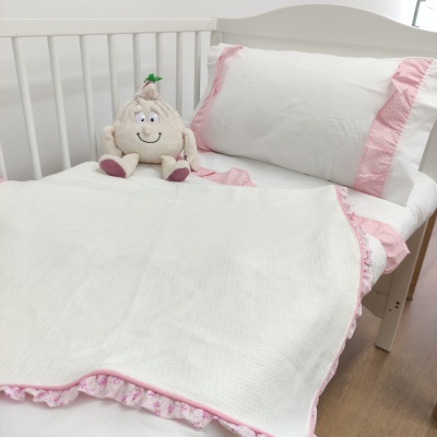 Cama de bebé com roupa de cama branca e rosa e boneco de alho de peluche.