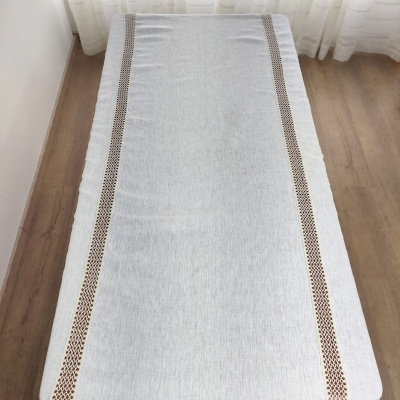 Toalha de mesa branca com faixas decorativas castanhas num ambiente com chão de madeira e cortinas brancas