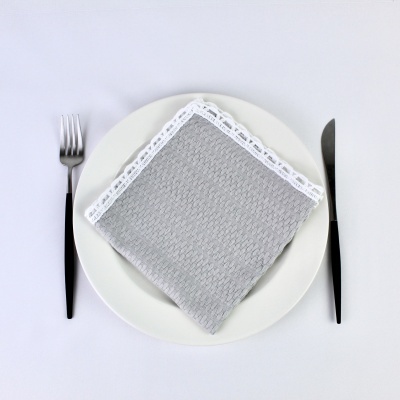 Guardanapo cinzento com renda branca num prato branco com talheres preto