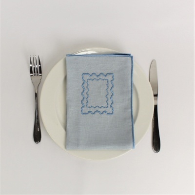 Prato branco com guardanapo azul bordado e talheres prateados num fundo branco