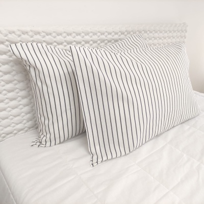 Duas almofadas riscas pretas e brancas sobre cama branca com cabecalho texturado branco