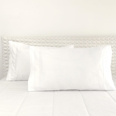 Dois almofadões brancos com fronhas bordadas em cama branca