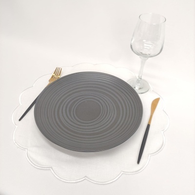 Prato cinzento cerâmico com talheres dourados e pretos, guardanapo branco floral e copo de vidro