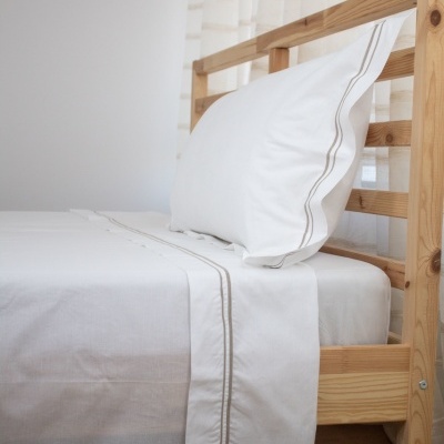 Cama de madeira clara com roupa de cama branca bordada em cinzento