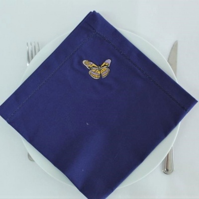 Guardanapo azul escuro com bordado de borboleta sobre prato branco entre talheres