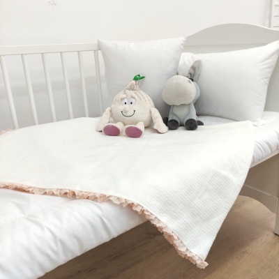 Berço branco com cobertor branco de borda rosa e duas peluches, uma de batata sorridente e outra cinzenta parecida com burra