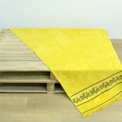 Tapete amarelo com padrão bordado verde escuro e franjas sobre paletes de madeira