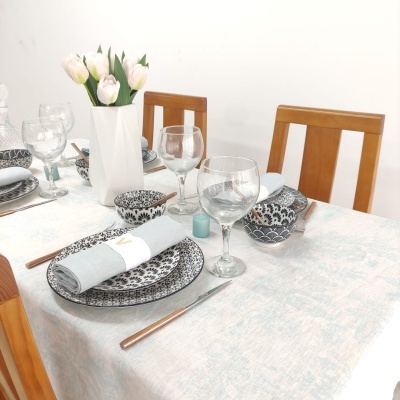 Mesa posta com pratos de porcelana, copos de vinho, guardanapos cinza e vaso branco com flores