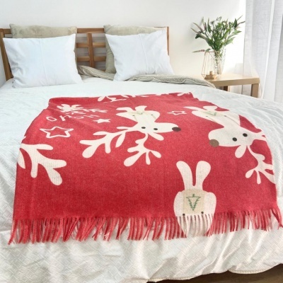 Cobertor vermelho com padrão de rena branca sobre cama em quarto minimalista