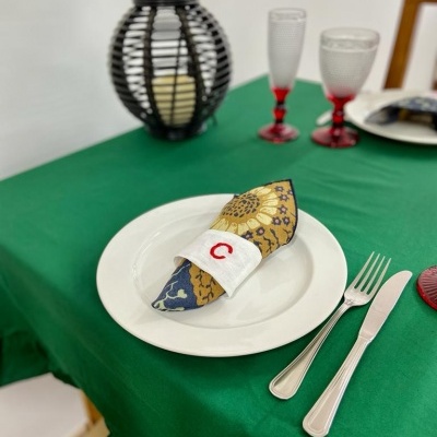 Mesa posta com toalha verde, prato branco, guardanapo estampado, talheres e copos vermelhos