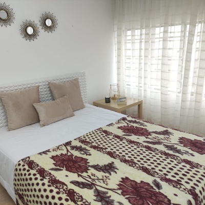 Cama com manta floral vermelha e almofadas castanhas perto de janela com cortinas brancas