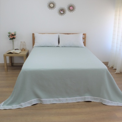 Cama com colcha verde-água e almofadas brancas num quarto minimalista com decoração simples