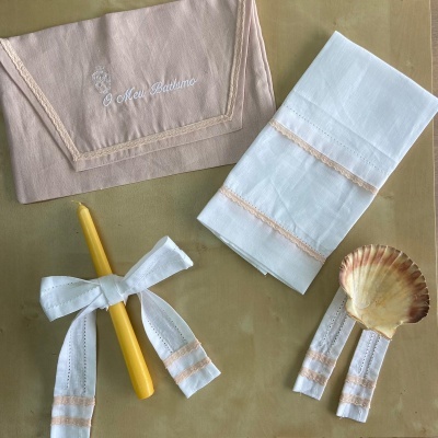 Toalhas bordadas em linho, vela amarela com fita branca bordada, concha decorativa sobre mesa bege