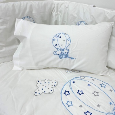 Conjunto de roupa de cama branca com bordados azuis e cinzentos de balões e estrelas