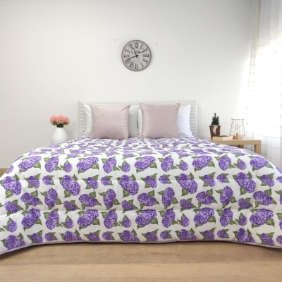 Colcha branca com flores lilás e folhas verdes numa cama com almofadas cor de rosa e brancas