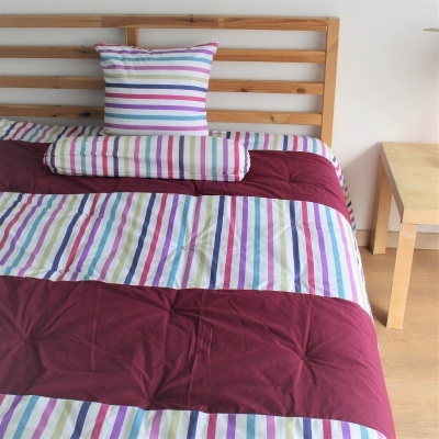 Conjunto de roupa de cama riscas coloridas e vinho numa cama de madeira com mesa ao lado