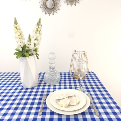 Mesa posta com toalha azul e branca, flores em vaso branco, garrafa de vidro, candelabro dourado, prato com pastelaria e copo de vinho.