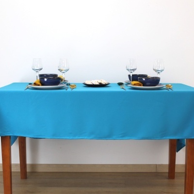 Mesa de madeira com toalha azul, pratos, tigelas, talheres, guardanapos e copos