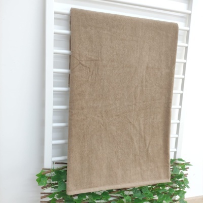 Toalha bege pendurada em estrutura branca com folhas verdes na base