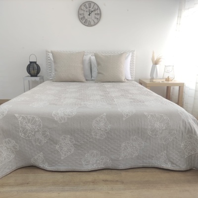 Cama de casal com colcha cinza com padrão de folhas e duas almofadas