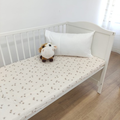 Cama de criança branca com lençol estampado, almofada branca e peluche de vaca