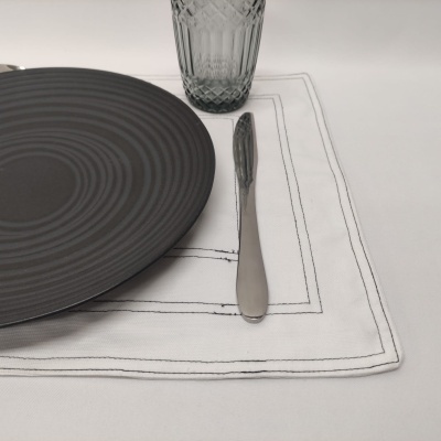 Prato cinzento, copo de vidro transparente e faca de metal em guardanapo branco bordado.