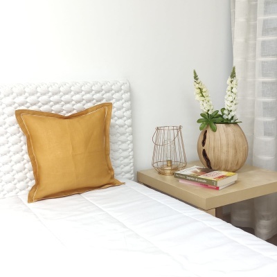 Almofada amarela numa cama branca junto a mesa de cabeceira com vaso, livros e decoração