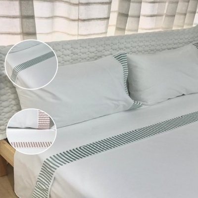 Roupa de cama branca com bordados riscado verde em cama com cabeceira acolchoada e cortinas claras