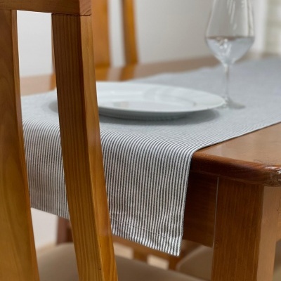 Mesa de madeira clara com toalha cinza riscada, prato branco e copo de vidro