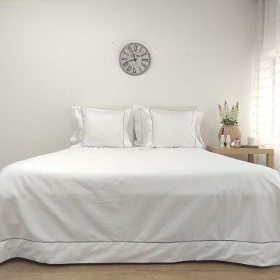 Cama com roupa de cama branca, almofadas, relógio de parede, mesa de cabeceira com vaso e flores