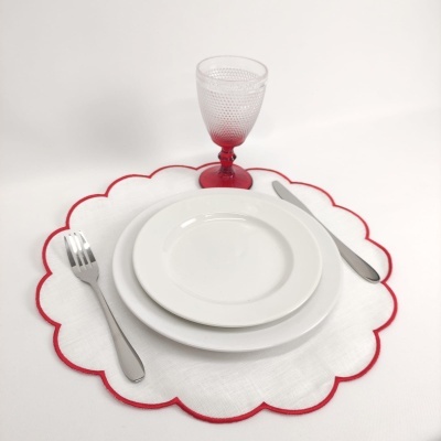 Conjunto de serviço de mesa com pratos brancos, cálice de base vermelha, talheres de metal e individual branco com borda vermelha