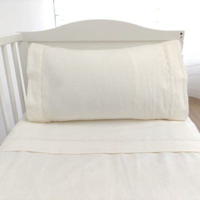 Almofada branca longa em cama de grades brancas com lençol branco num quarto claro