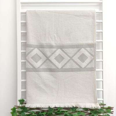 Toalha de banho branca com padrão cinzento pendurada numa estrutura branca com folhagem