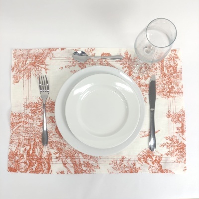 Conjunto de jantar com prato branco, talheres metálicos, copo de vidro e base de tecido estampado vermelho.