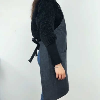 Avental cinzento escuro em tecido amarrado nas costas com roupa preta por baixo