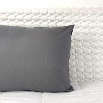 Travesseiro cinzento sobre colchão branco junto a cabeceira acolchoada branca