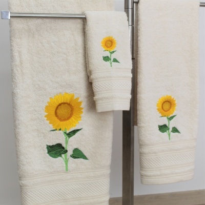 Três toalhas cor creme com bordado de girassol penduradas em suporte metálico