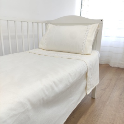 Cama de solteiro branca com roupa de cama creme e almofada decorativa com renda