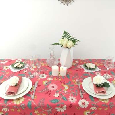 Mesa de jantar decorada com toalha floral vermelha, pratos brancos, guardanapos cor de rosa e flores brancas