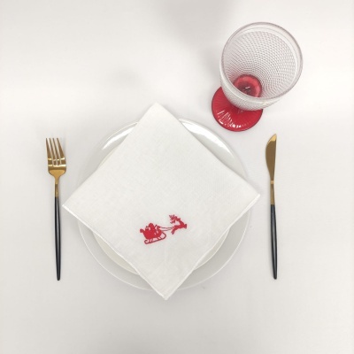 Conjunto de mesa com prato branco, guardanapo bordado, talheres dourados e copo com base vermelha