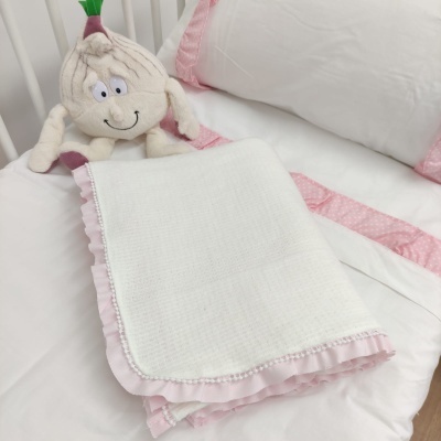 Lenço branco com barra rosa sobre cama branca com detalhes rosa e almofada de cebola de tecido