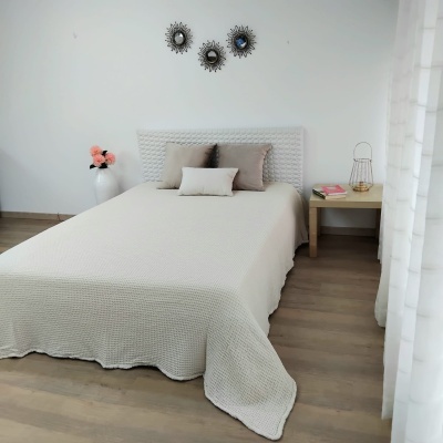 Cama com colcha bege texturizada e almofadas neutras numa divisão minimalista