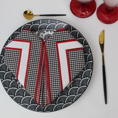 Prato redondo com padrão preto e branco, guardanapo xadrez preto, branco e vermelho, talheres dourados com cabo preto e dois copos vermelhos